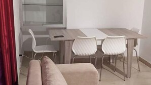 Una sala moderna con un sofá beige, una mesa de comedor con sillas y un aparador de vidrio.