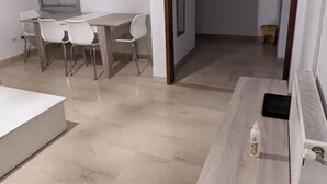 Una habitación moderna y luminosa con una mesa de comedor de madera y sillas, una pequeña cocina americana y un espejo grande en la pared.
