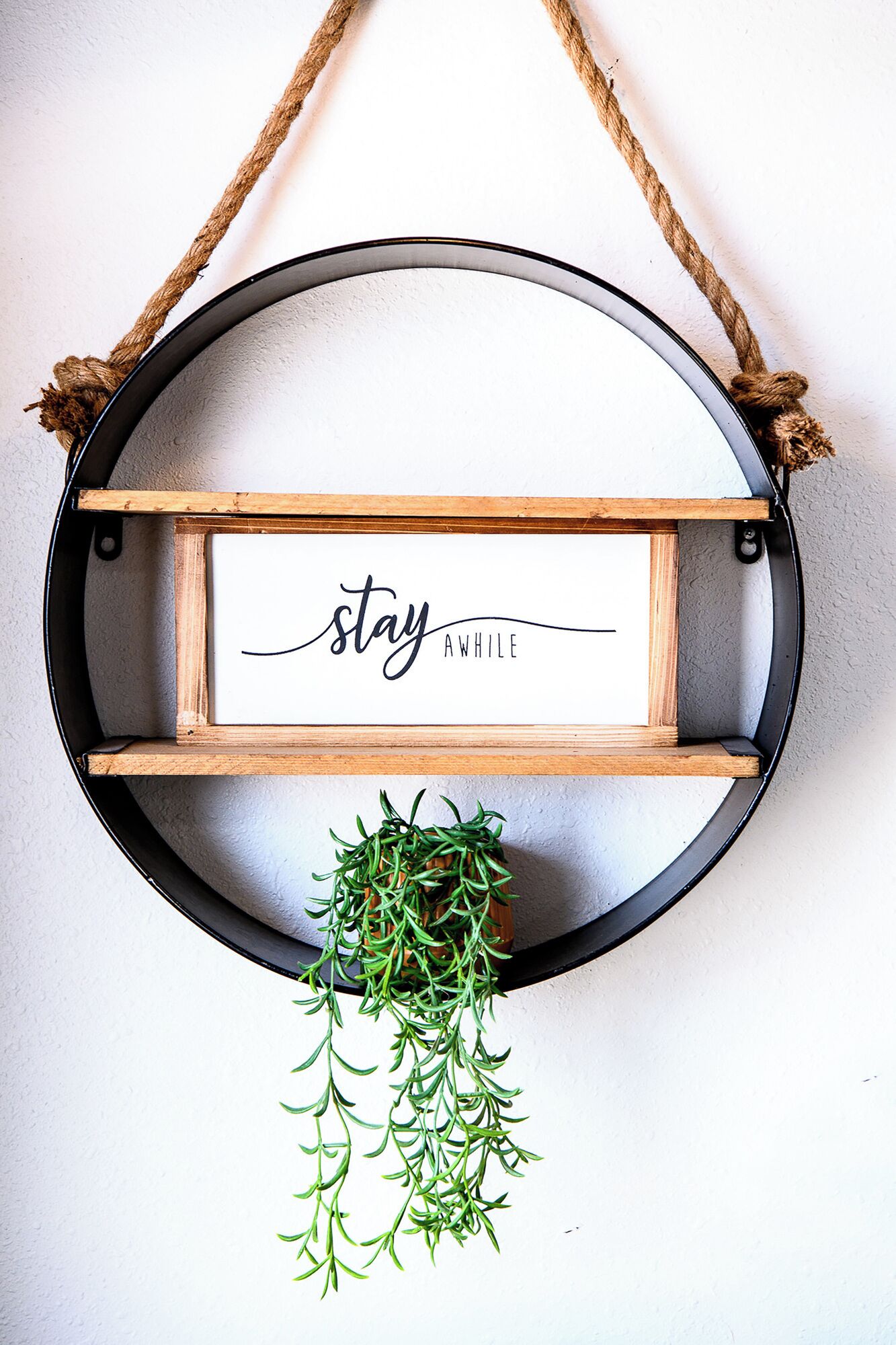 A circular wall hanging with a wooden frame, a motivational quote, and a hanging plant.