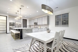 A modern kitchen with white cabinetry, stainless steel appliances, and pendant lighting. - Estrella Mountain 5 Bdrm w/Views, Pool, and Games! (Goodyear)