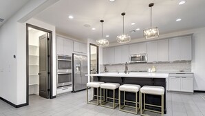 Una cocina moderna con gabinetes blancos, electrodomésticos de acero inoxidable y una zona de bar con taburetes.