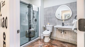 A modern bathroom with a glass shower enclosure, a toilet, a sink with a mirror, and marble flooring. - Melwood Suites Unit 106 Studio (Pittsburgh)