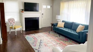 Una sala de estar con chimenea, un sofá azul, un tapete estampado y un televisor en la pared.