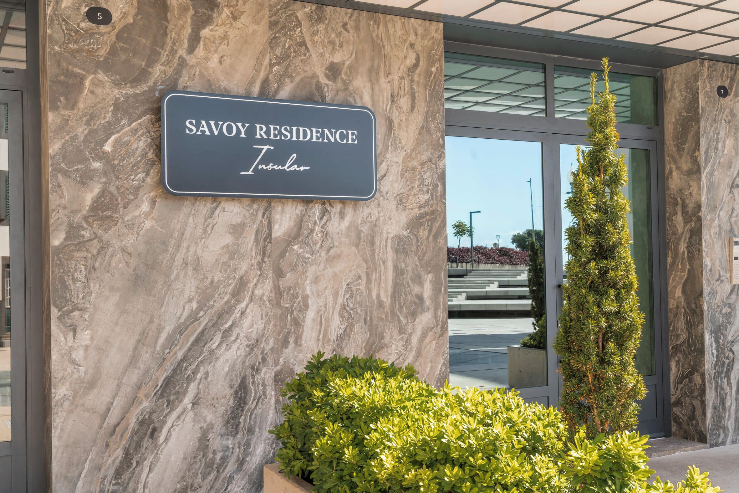 Señalización para 'Savoy Residence', con una pared de mármol y una planta alta y delgada al frente.