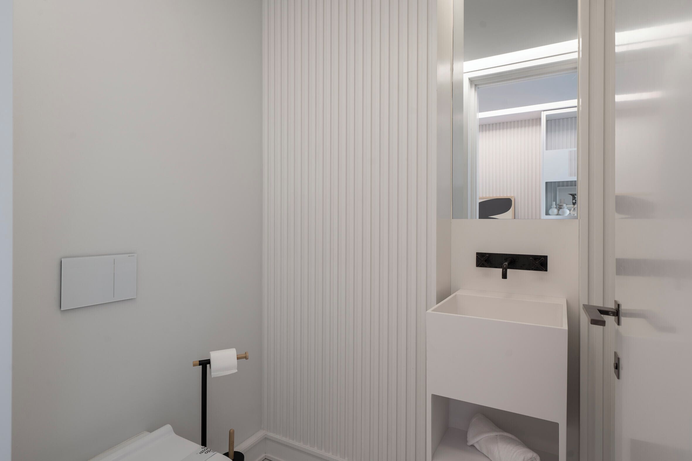 A modern bathroom with a white sink, a mirror, and a toilet.