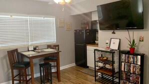 A compact kitchen with a dining table, chairs, a refrigerator, a flat-screen TV, and a bookshelf. - The Unique cozy studio (Winter Haven)