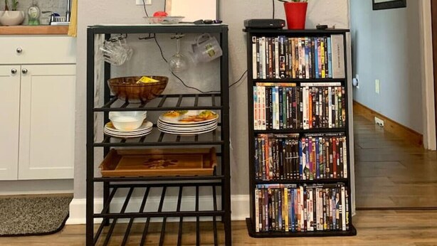 A living room with a flat-screen TV mounted on the wall, a bookshelf filled with books, and a small table with a bowl and plates. - The Unique cozy studio (Winter Haven)