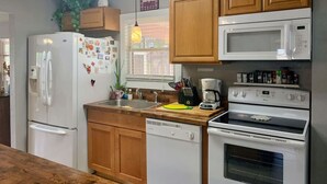 Eine Küche mit Holzausstattung, einem Kühlschrank, einer Mikrowelle, einem Backofen, einem Geschirrspüler und einem Fenster mit Jalousien.