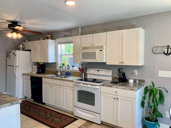 A kitchen with white cabinets, a stove, microwave, and a ceiling fan.