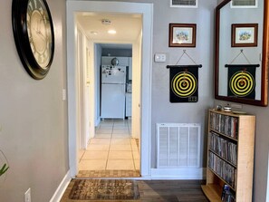 A hallway with a clock, a door leading to a kitchen, and a bookshelf with CDs.