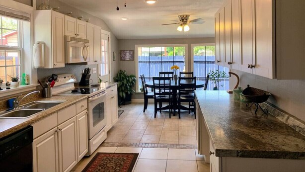 A kitchen with white cabinets, a dining table with chairs, and a ceiling fan.