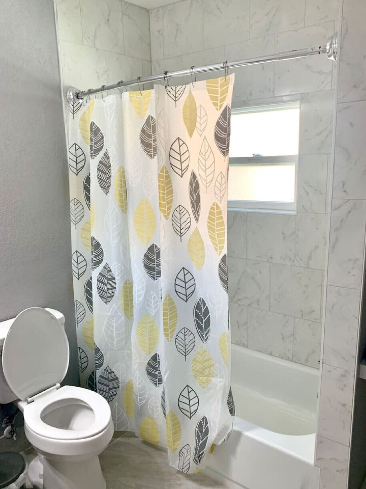 Une salle de bain avec un rideau de douche orné d’un motif de feuilles, des toilettes blanches et une baignoire.