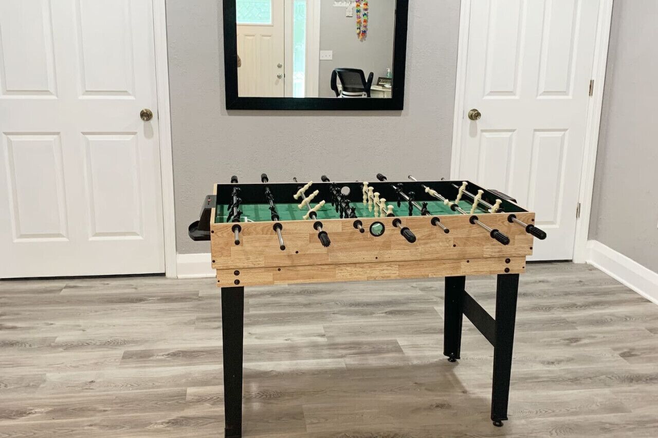 A wooden foosball table in a room with light gray walls and white doors.