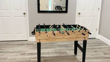 A wooden foosball table in a room with light gray walls and white doors.