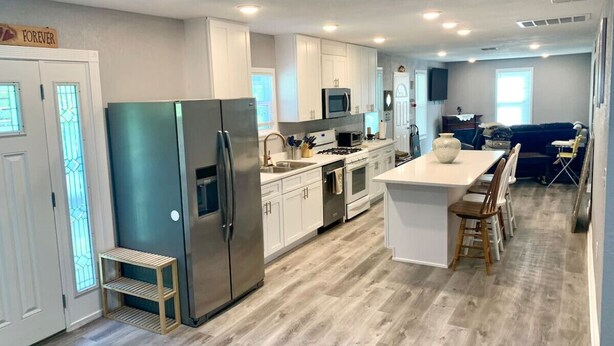 Una cocina moderna con armarios blancos, electrodomésticos de acero inoxidable y una isla central con taburetes de bar.