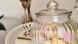 A glass jar with a lid filled with colorful candies, placed on a white plate with a floral design. - Strategic location and cozy atmosphere for a perfect Roman vacation. (Roma)