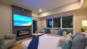 Una habitación de hotel moderna con una cama grande, un sofá, un televisor montado en la pared, una chimenea y vistas al mar a través de las ventanas.