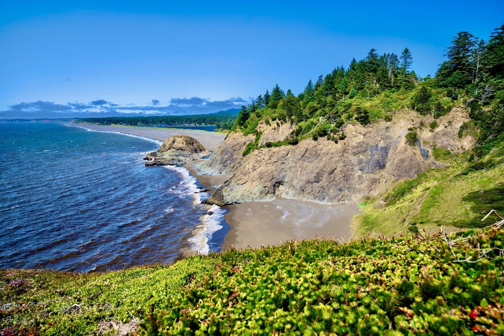 Un paysage côtier comprenant une plage, des falaises rocheuses et une forêt dense.