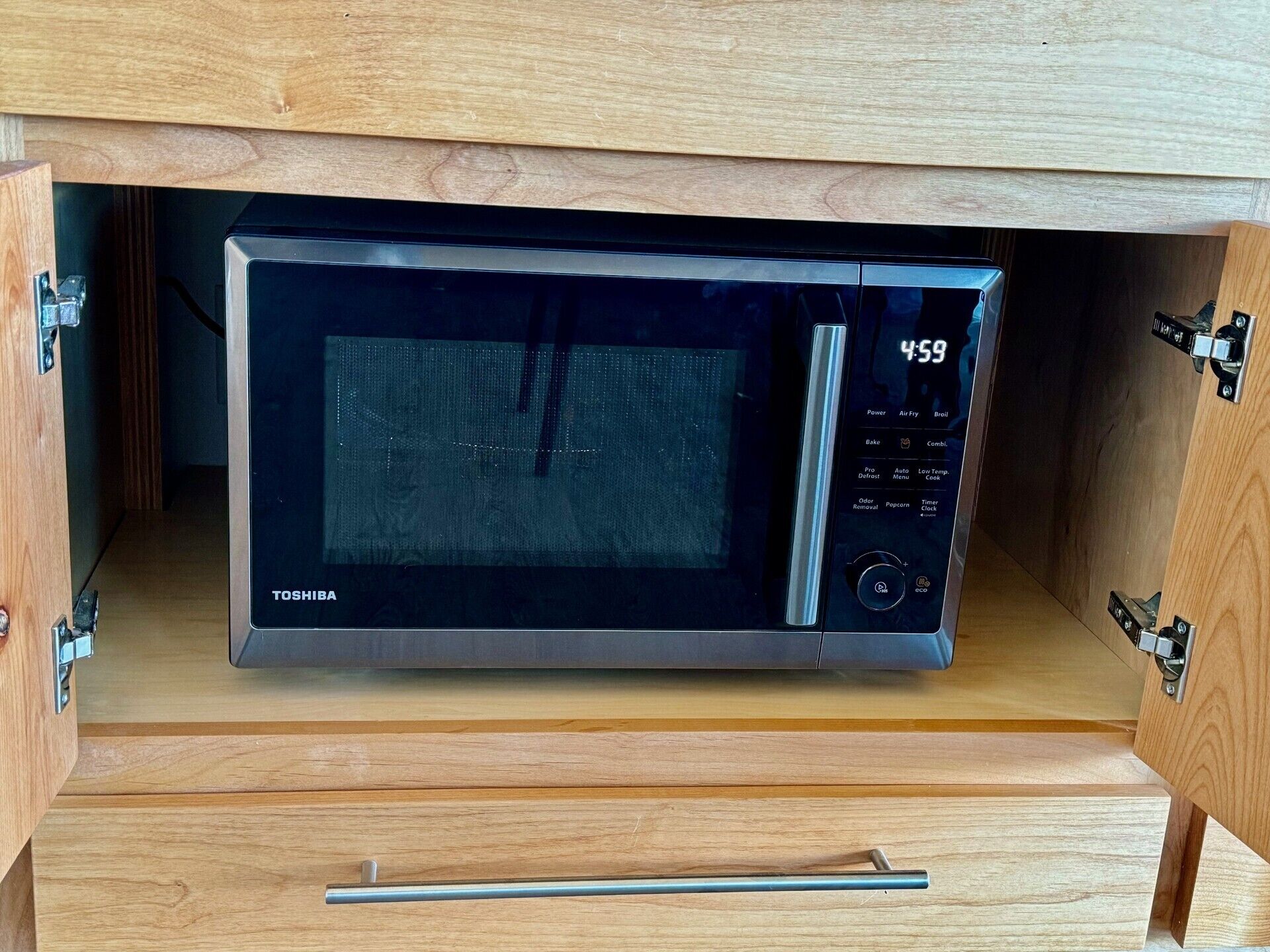 A Toshiba microwave oven installed in a wooden cabinet with a drawer below.
