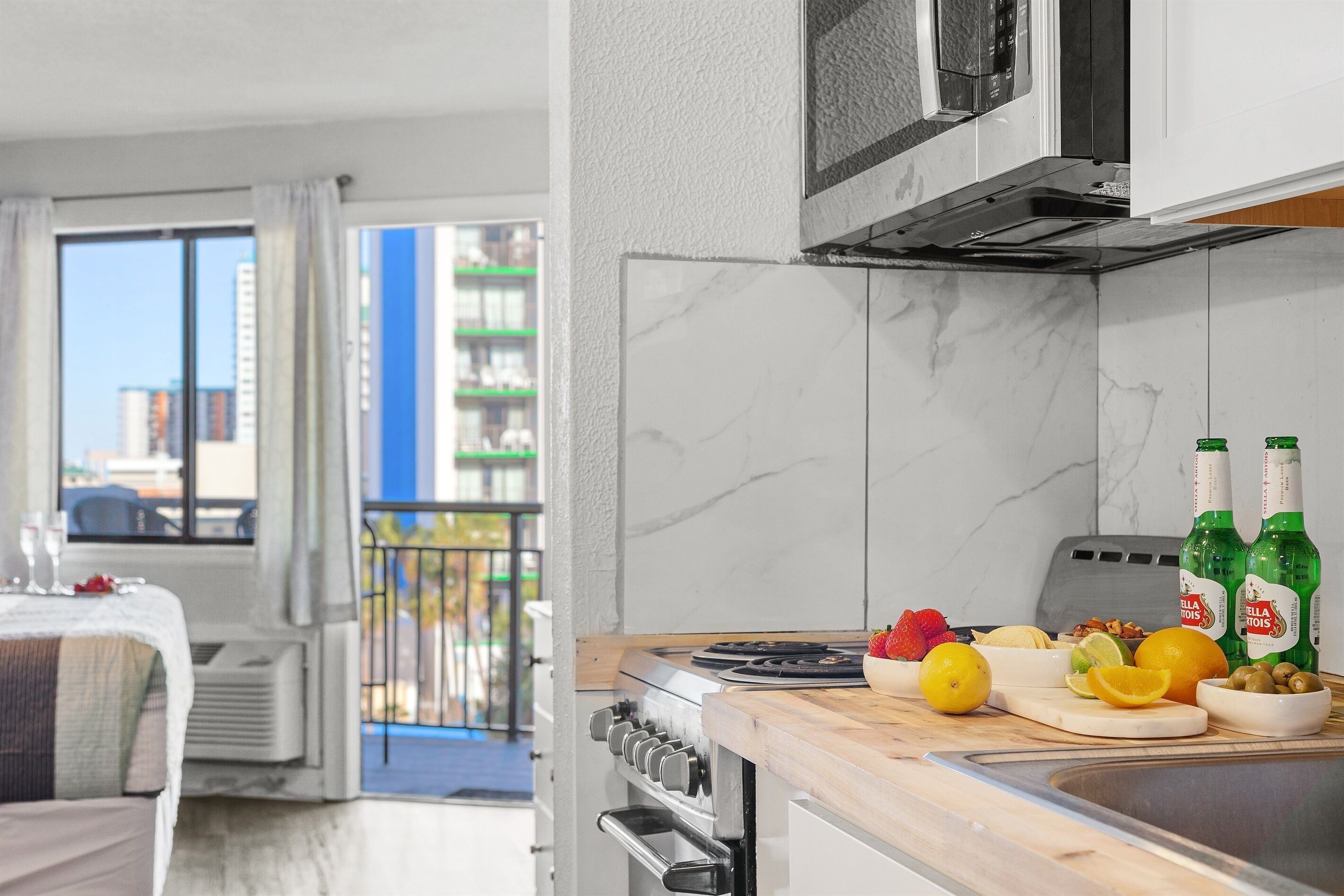 A modern kitchen with a stove, microwave, and marble backsplash. There are fruits and bottles on the counter.