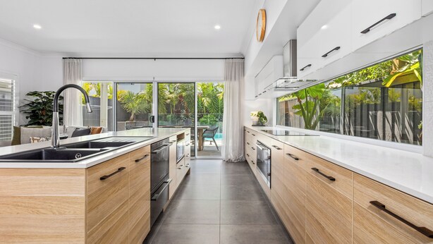 Une cuisine moderne dotée d’un îlot central, de meubles en bois et offrant une vue sur un jardin grâce à de grandes fenêtres.