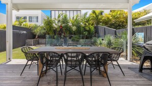 Une terrasse extérieure avec une table rectangulaire et six chaises, entourée d’une plateforme en bois et d’une rambarde en verre.