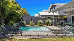 Un jardin avec une piscine, une terrasse en bois et des chaises longues.