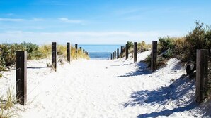 Un sentier de sable bordé de poteaux en bois, qui mène à l’océan.