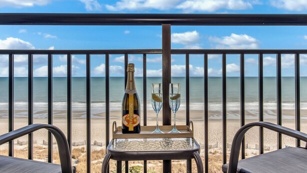 Un balcon avec vue sur la plage, une bouteille de champagne et deux verres sur un plateau.