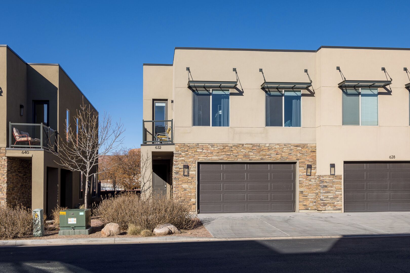Un bâtiment moderne à deux étages, doté d’une façade en pierre, d’un garage et d’un balcon avec espace salon extérieur.