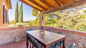 Un porche cubierto con pared de ladrillo, una mesa de madera y sillas verdes.