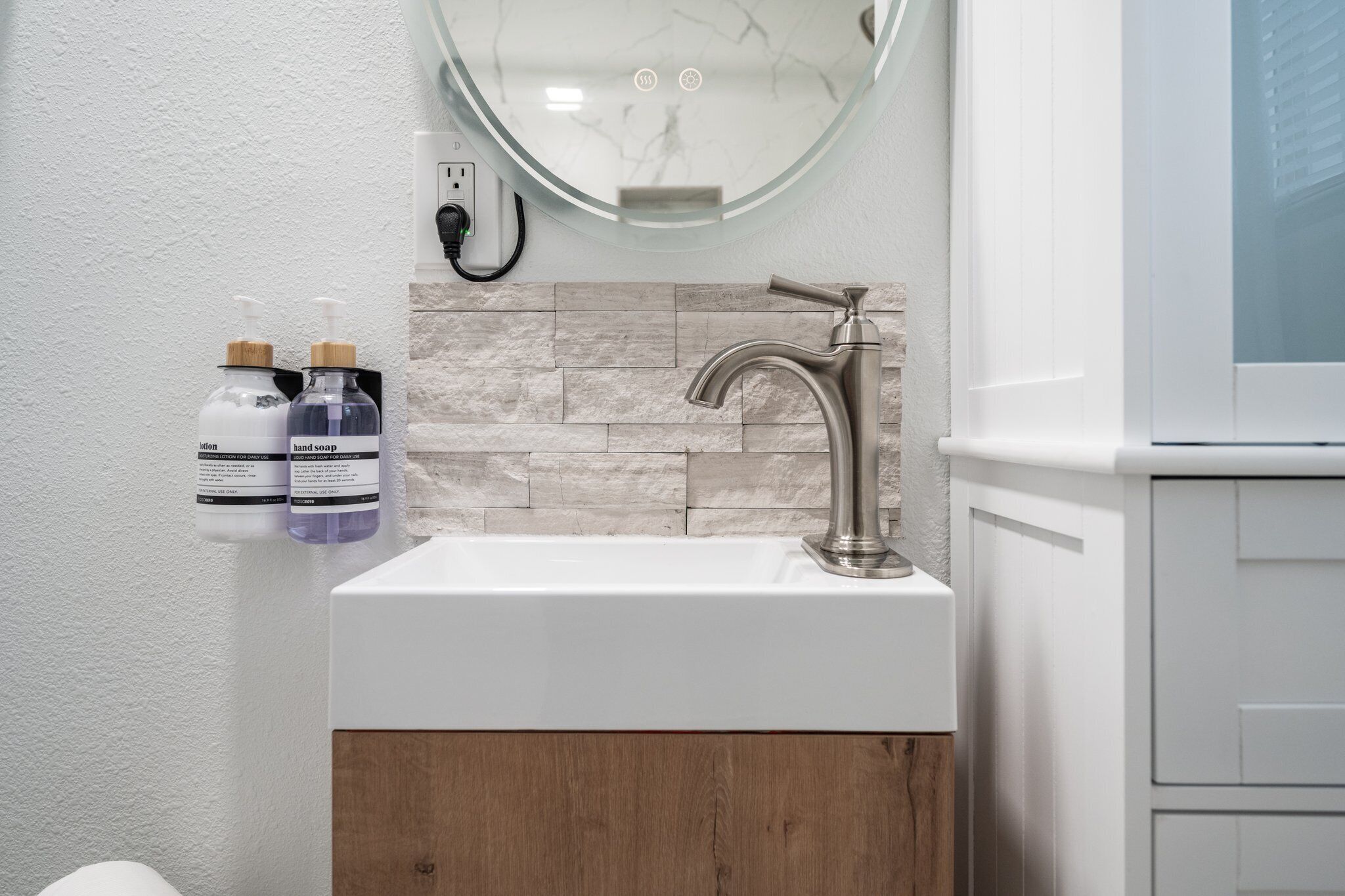Un bagno moderno con un lavabo in marmo, un mobile in legno e due erogatori di sapone per le mani.