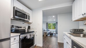 Una cocina moderna con electrodomésticos de acero inoxidable, armarios blancos y piso de madera.