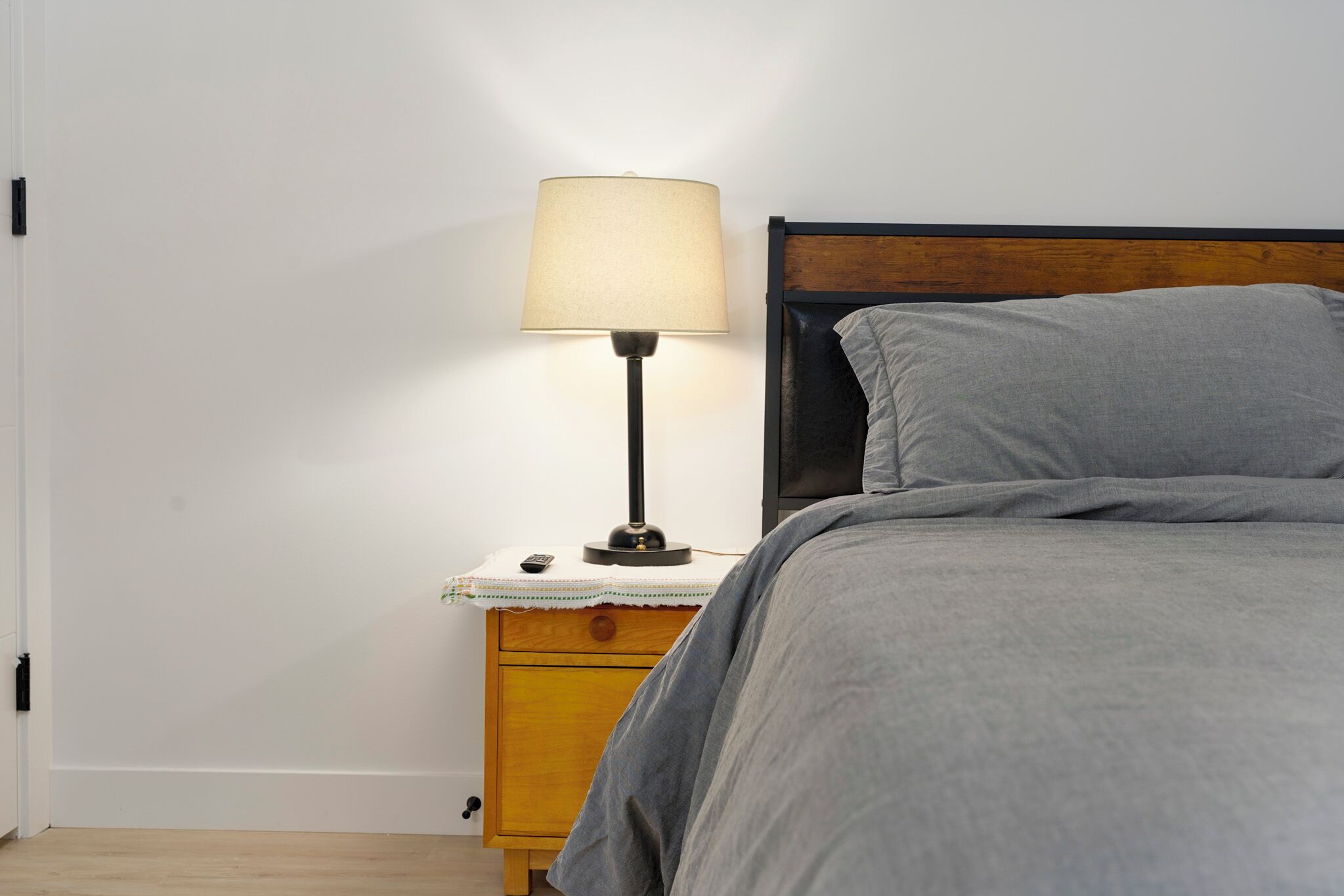 A bedroom with a bed, a nightstand, a lamp, and a wooden headboard.