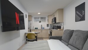 A compact living space with a kitchenette, a sofa, a small dining table, and a TV mounted on the wall. - Modern Suite Near Royal Alex Hospital, LRT, Rogers|Free WiFi, Parking & Netflix (Edmonton)