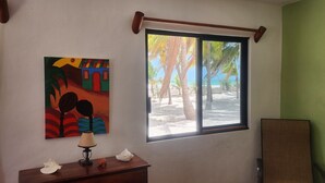 A room with a window overlooking a beach, a painting on the wall, and a small table with a lamp and decorative items. - Ocean Front, Accessible, 3-bdrm Home!  (Celestún)