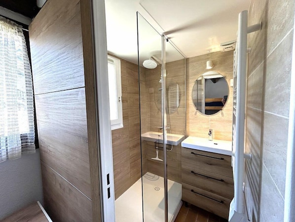 A modern bathroom with a glass shower enclosure, a round mirror, and a wooden vanity.