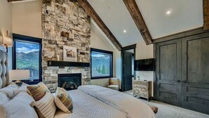 A bedroom with a stone fireplace, a large bed with multiple pillows, a dresser, and a wardrobe. - Heaven`s Gate Luxury Ski-In/Out in Lewis Ranch (Copper Mountain)