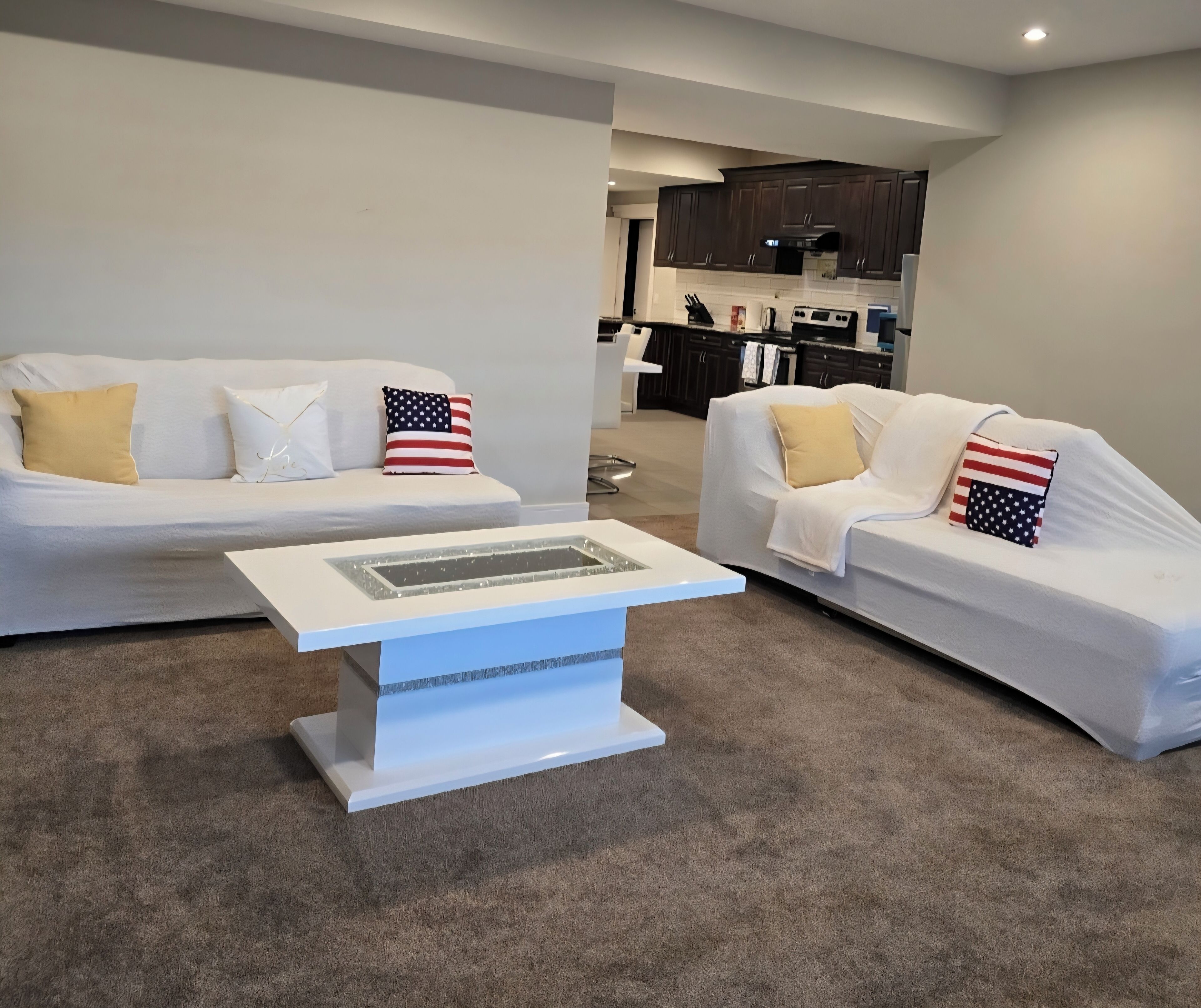 Sala de estar com dois sofás brancos, uma mesa de centro e almofadas com a bandeira americana.