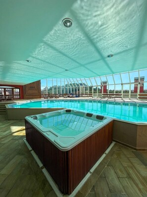 A large indoor swimming pool with a hot tub, wooden flooring, and a glass ceiling. - Suíte Luxo no Hotel Quatre Saisons   (Campos do Jordão)