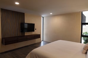 A modern bedroom with a large bed, a TV mounted on a wooden panel, and a window providing natural light.
