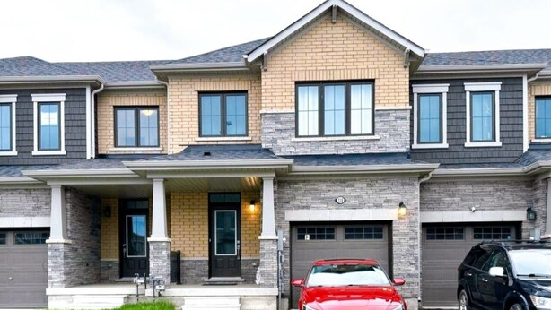 Une maison à deux étages avec un porche à l’avant, un garage et deux voitures garées dans l’allée.