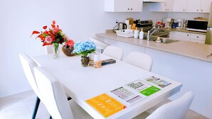 Une cuisine moderne avec des meubles blancs, une table à manger avec des chaises et un vase rempli de fleurs.