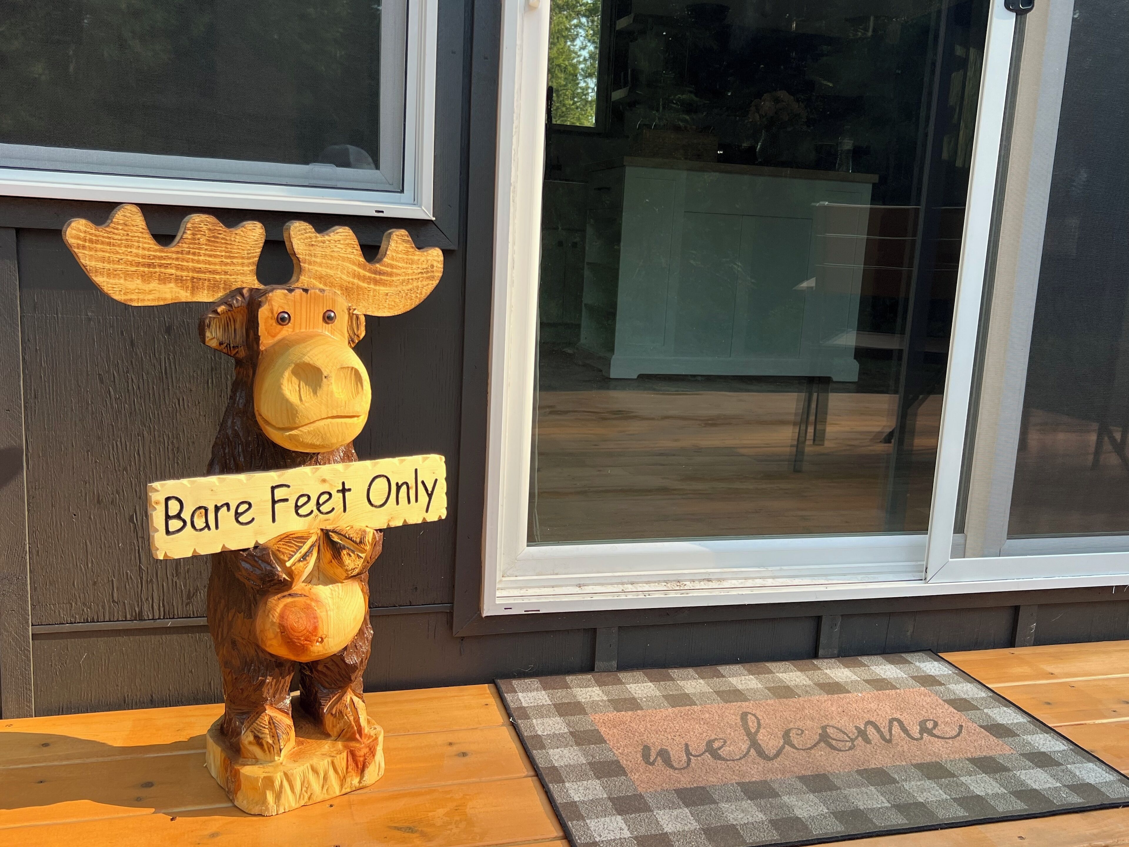 A wooden moose sculpture with a sign that reads "Bare Feet Only" in front of a building with large windows.