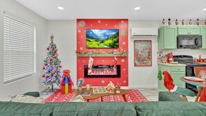 Een woonkamer met een open haard, een kerstboom en een keuken met groene kastjes.