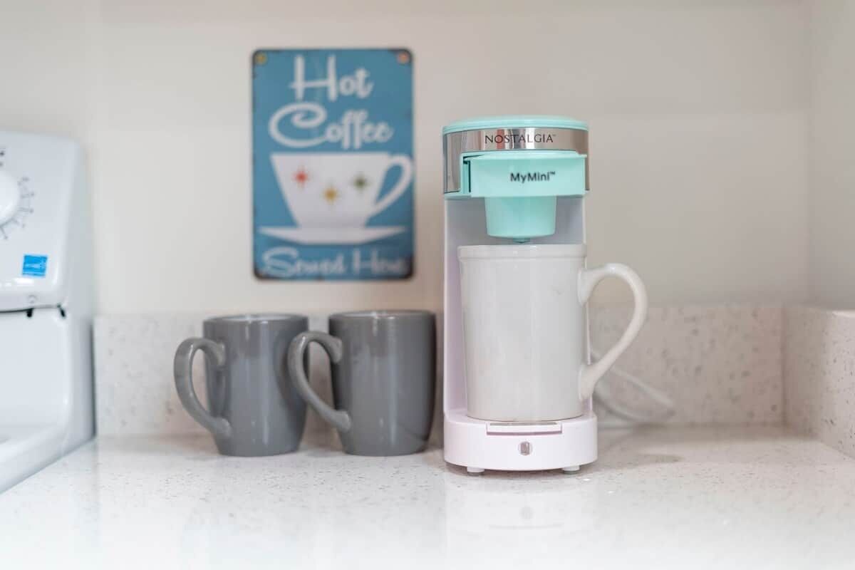 Eine Kaffeemaschine mit MyMini™-Spender auf einer Arbeitsplatte, zwei graue Tassen und ein Schild mit der Aufschrift 'Hot Coffee' im Hintergrund.