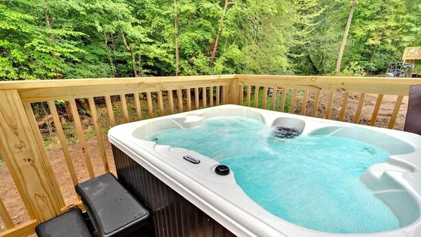 Un bain à remous sur une terrasse en bois, avec une balustrade en bois, entouré d’arbres.