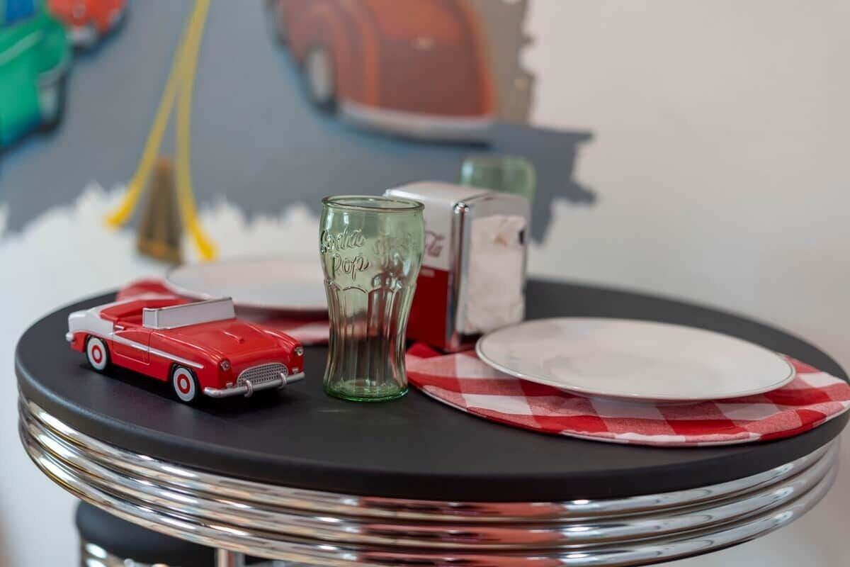 Une table avec une petite voiture rouge, un verre vert et une serviette à carreaux.