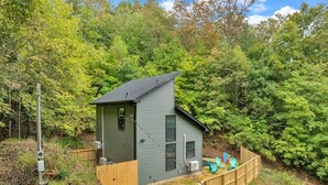 Eine kleine, eingeschossige Holzhütte mit umzäuntem Garten, umgeben von dichtem Wald.