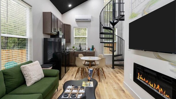 Ein moderner Wohnraum mit einem grünen Sofa, einem Essbereich, einer Küche, einem Kamin und einer schwarzen Wendeltreppe.